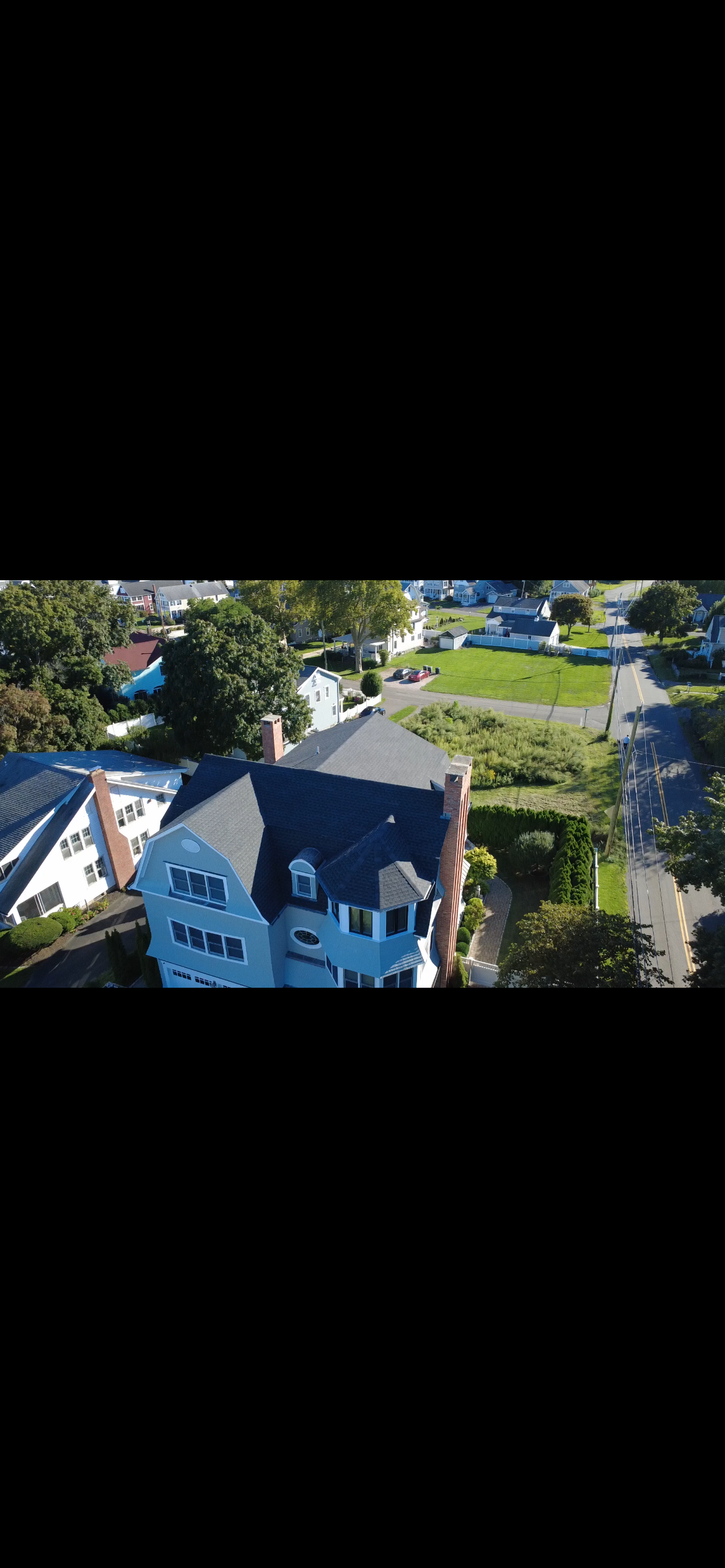 Drone photo of a three-story shoreline home with a dark gray shingle roof