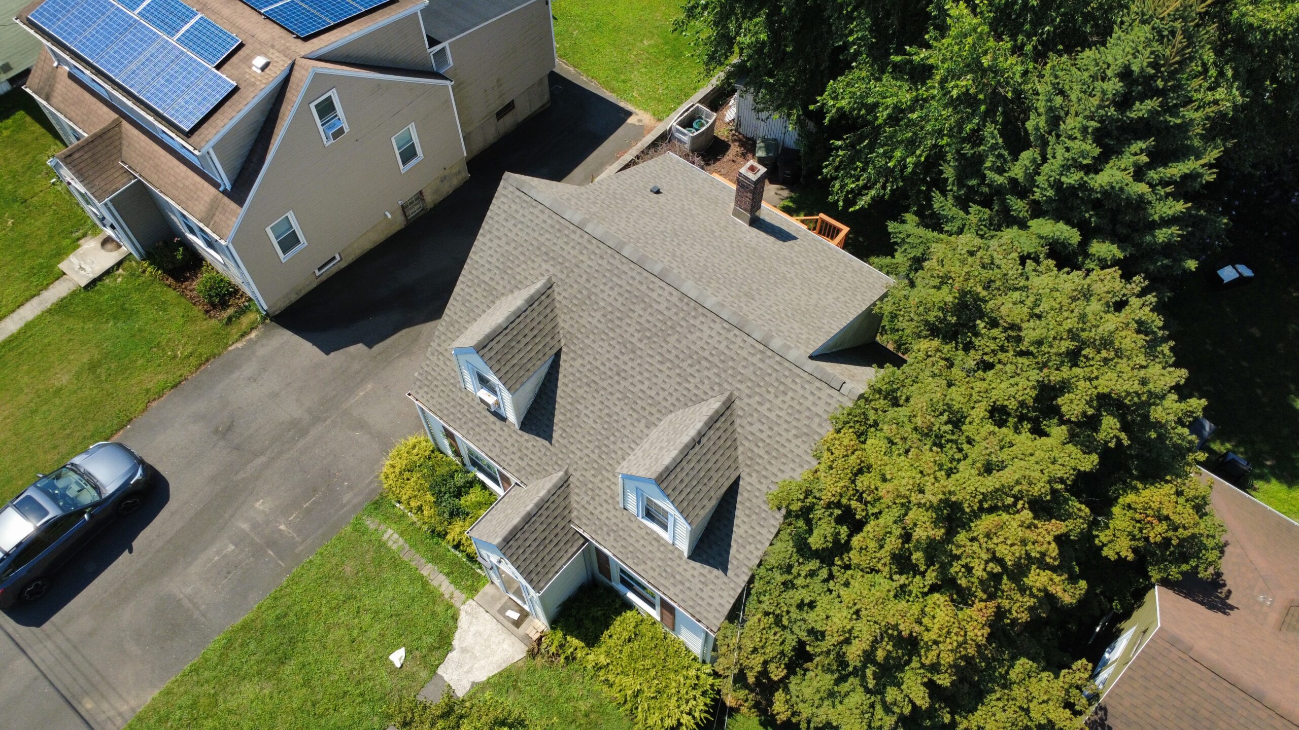 Gray architectural shingle roof with two front dormers, drone view